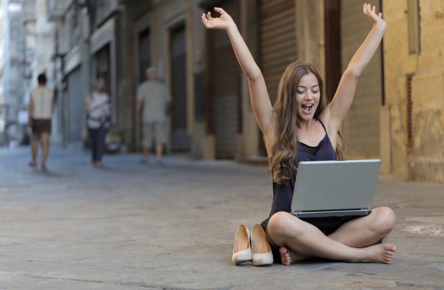 woman raising her hands up while sitting on floor with macbook pro on lap